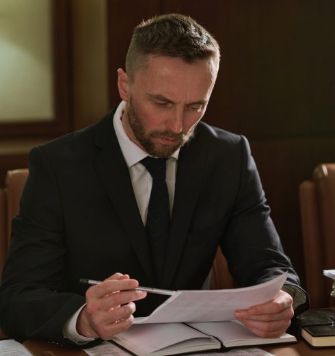 Confident male notary or lawyer in suit pointing at business contract and looking through terms and conditions in boardroom