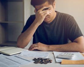 Asian men are stressed about financial problems, with invoices and calculators placed on the table while having stress on problems with home expenses.
